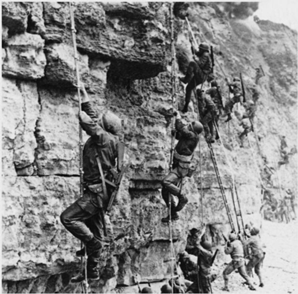 A black and white photo of D-Day soldiers climbing Point Du Hoc