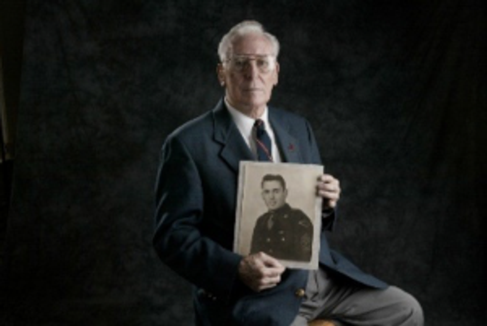 Bud Lomell poses with a portrait from his days in the Army.