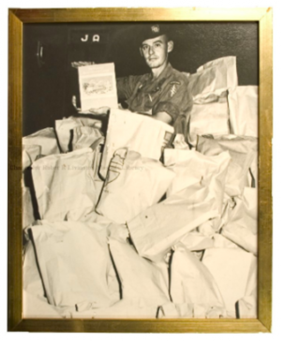 A photograph (in a gold-painted frame) of a United States Vietnam War soldier in the middle of a pile of Masonic Gift Packages.